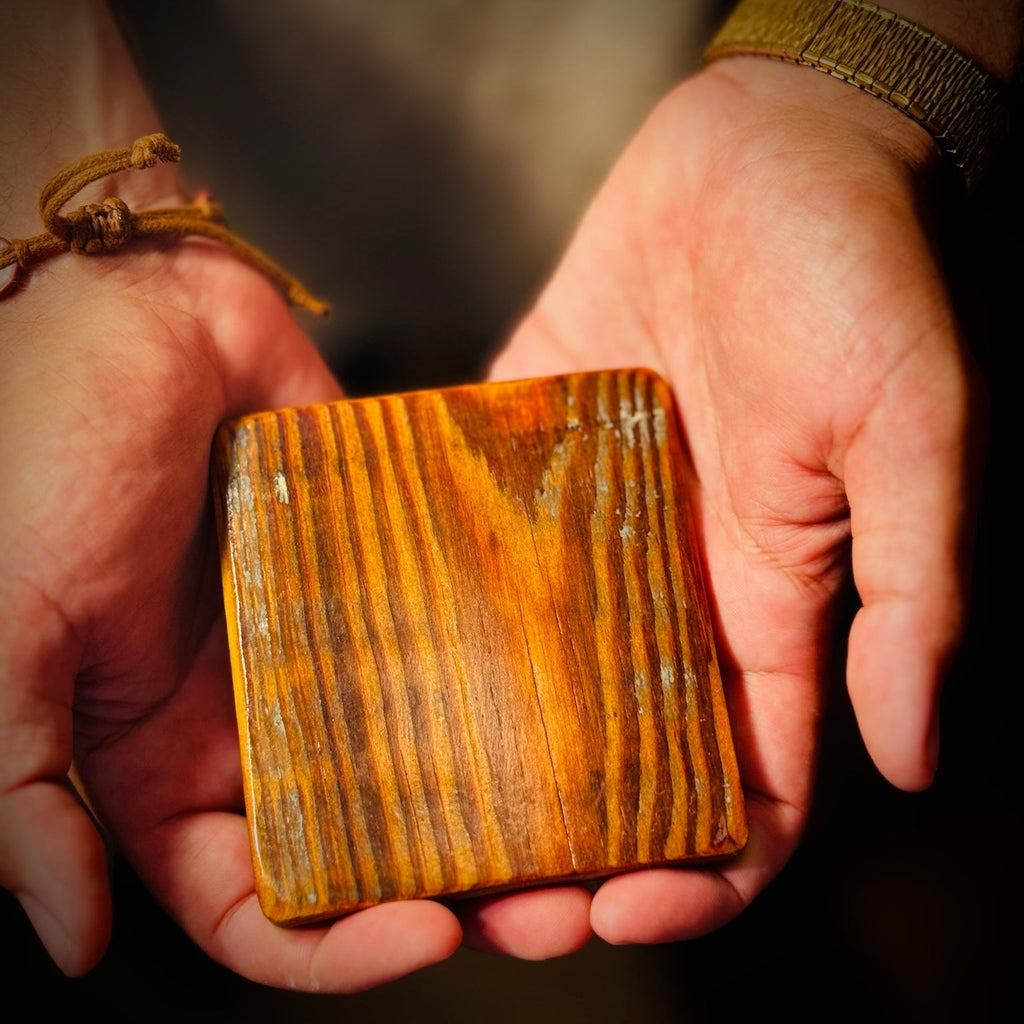 Single handmade reclaimed heart pine coaster held in both hands showing grain and old paint